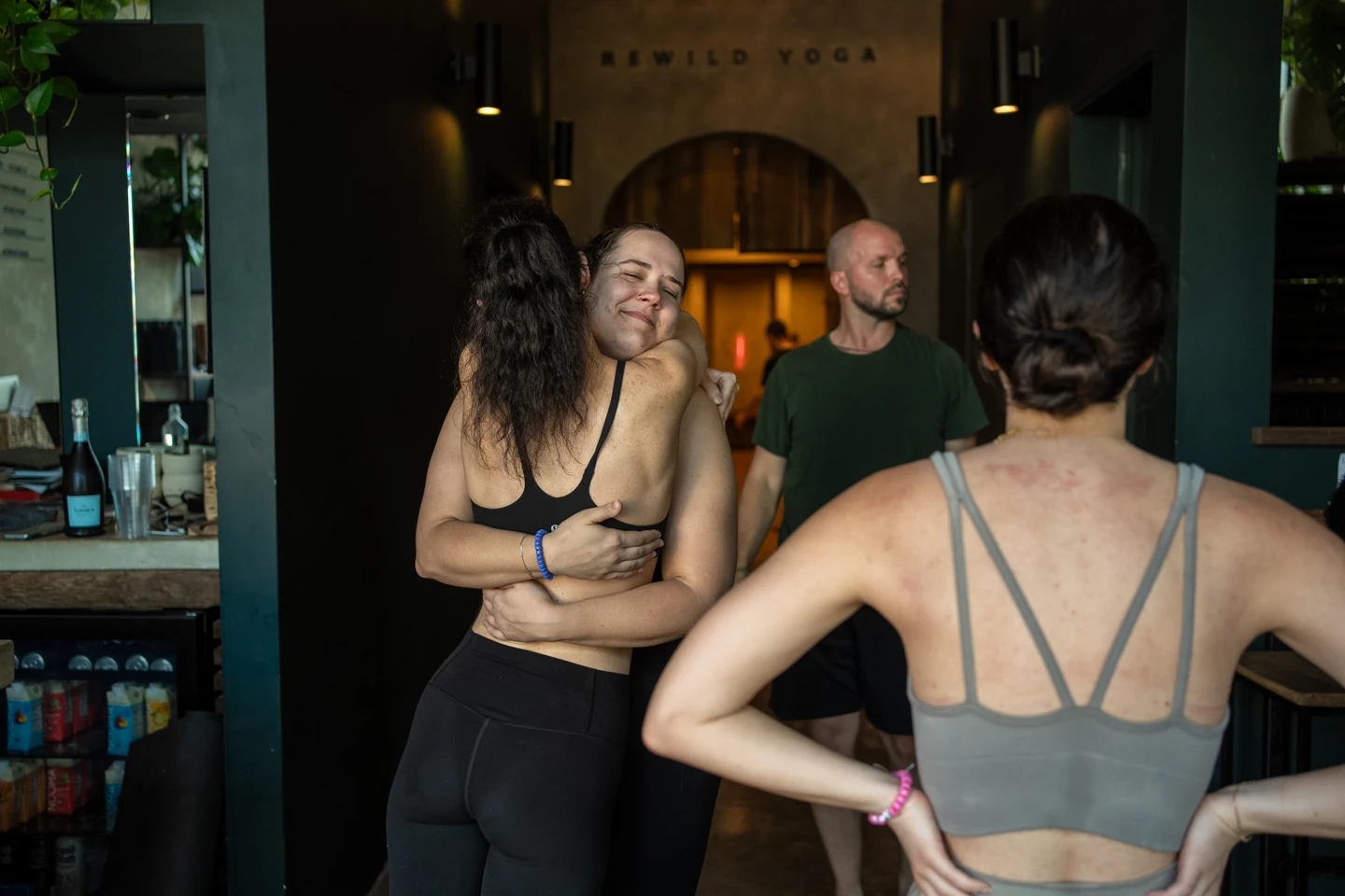Community members hug and talk beside the studio’s wooden arch after class.