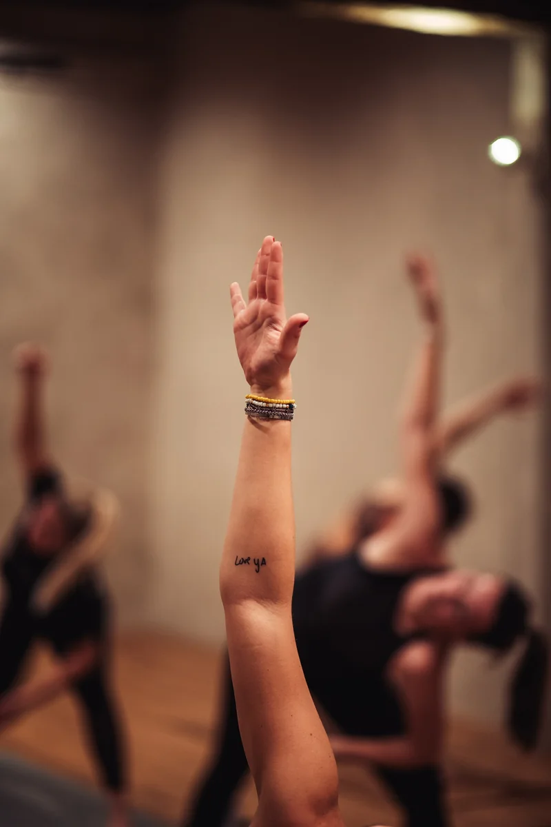A raised hand and forearm in focus, with a class softly blurred behind.
